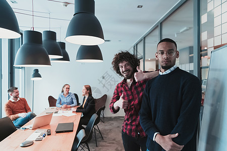 现代办公室中两个快乐的千禧一代男性企业主的肖像 两个商务人士微笑着看着相机 忙碌的多元化团队在后台工作 领导概念 爆头讨论合作教图片