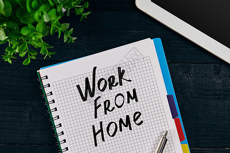 用“在家工作”题词书写的开放式笔记本的顶视图 绿色的花 平板电脑 笔和木制背景上的笔记本图片