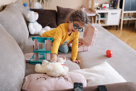 可爱的小女孩在她的房间里扮演医生 可爱的三岁女孩花时间玩耍 戴眼镜的女孩黄色上衣和蓝色紧身裤 乌克兰可爱的孩子 她的孩子厨房的背图片
