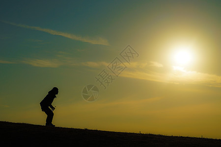 黄昏时站在山丘上的男人的休眠太阳草原爬坡日落例子男性阴影三鹰公园橙子图片