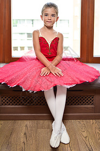 一个美丽的小芭蕾舞女的肖像 穿着一身红礼服 坐在窗边 梦想成为职业芭蕾舞舞蹈者图片
