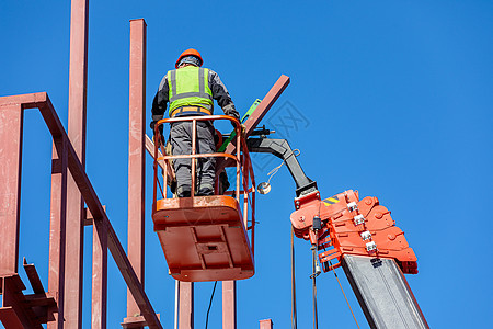 雄男性建筑工在抬起摇篮的高度工作 创建了大楼铁架高个子安全帽钢材工具水力学电梯作品男人专业人员工作服图片