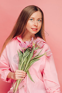 一个甜美迷人的女人 在粉红色的背景上穿着粉红色的裙子 微笑 幸福和幸运情感喜悦女孩展示礼物花束快乐花朵女士工作室图片
