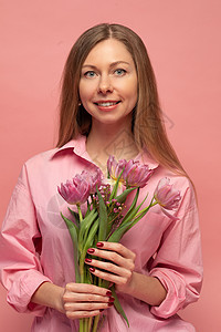 一个甜美迷人的女人 在粉红色的背景上穿着粉红色的裙子 微笑 幸福和幸运冒充女士工作室快乐成人花朵情感礼物展示青年图片