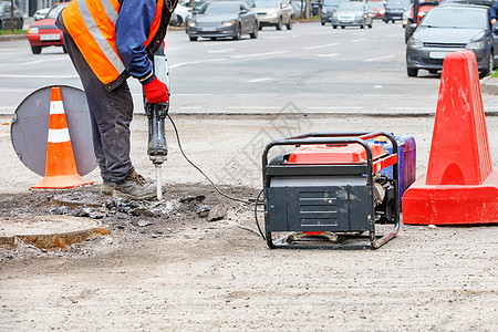 一名穿反光服装的公路工人用电动大锤打碎路边的旧沥青图片