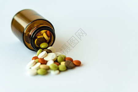 医学和药丸 在白色背景特写镜头的多色药物 有里面药片的棕色玻璃瓶在白色背景 从倒置的罐子中溢出到白色表面的多色药片卫生抗生素制药图片