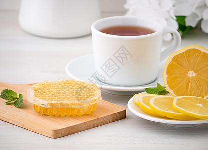 白杯加茶 柠檬片和蜂蜜在白色木制桌椅上的蜂窝中的蜂蜜叶子玻璃水果勺子桌子植物芳香香气杯子饮料图片