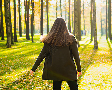 长着黑头发的女孩在公园里阳光照耀地旋转 女人站在她的背上 面对太阳 向前看图片
