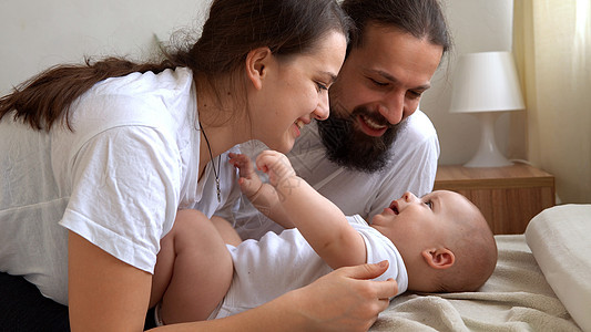 抱着新生儿的女人和男人 妈妈 爸爸和婴儿在床上 特写 年轻微笑的家庭画象有新生儿的在手上 背景的愉快的婚姻夫妇 童年 为人父母 图片