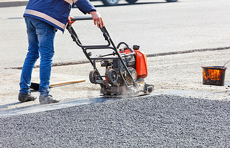 一名道路服务工人用车牌汽油振动器压紧沥青 修筑公路图片