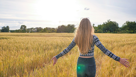 阳光麦田一个美丽的金发少女 穿过小麦田转过身 微笑着笑容背景
