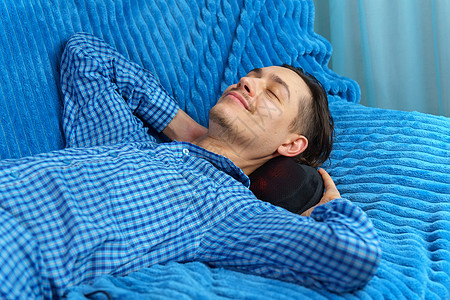 男人躺在沙发上 用电动按摩枕头按摩他的脖子图片