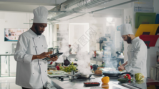 美国餐厅非裔美国人厨师在数字平板电脑上寻找美食食谱背景