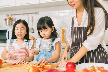 切水果游戏女孩在家里的厨房里享受与母亲和姐姐一起玩切苹果游戏快乐假期孩子素食主义者房间烹饪厨具儿童父母活动背景