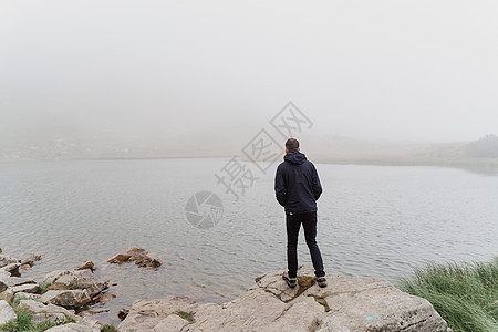 男子旅游者正在迷雾湖附近的岩石上旅行和站立 徒步登山并攀登到山顶 乌克兰的旅游业环境场地地形爬坡晴天国家旅游蓝色木头踪迹图片