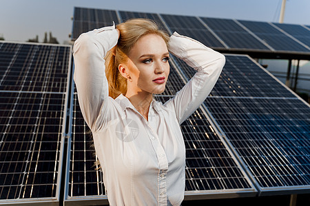 带太阳能电池板的金发模特在地上排成一排 穿着白色正装衬衫的女孩对着电厂微笑 绿色能源技术电气车站活力商业资源场地生态太阳能控制板图片