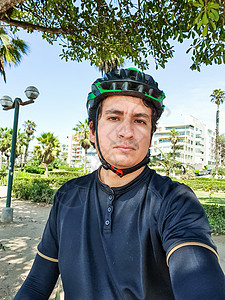 穿着黑色自行车服装的年轻英俊骑自行车者 在公园中戴头盔图片