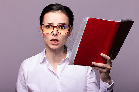 身着白衬衫和眼镜的女人手里拿着红色笔记本商务头发衬衫鬼脸美丽女性黑发学生商业秘书图片