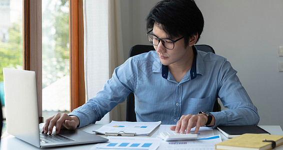 年轻亚洲男子手自由职业者的肖像正在现代办公室的平板电脑上工作 做会计分析报告房地产投资数据 财务和税收系统概念银行业花费人士经济图片