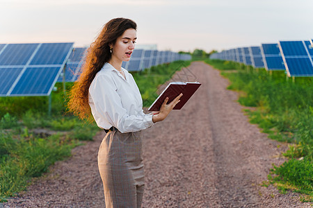 女性投资者穿着正式的白衬衫 在地面太阳能电池板上排行旁看书和阅读书发电厂活力环境电气光电池太阳阳光控制板商业光伏图片