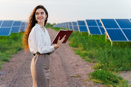 令人惊讶的女孩站在地上两排太阳能电池板之间阅读书本 地球的可持续性 绿色能源图片
