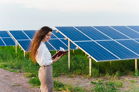 女性投资者穿着正式的白衬衫 在地面太阳能电池板上排行旁看书和阅读书光伏技术活力电压发电厂资源场地光电池工程商业图片