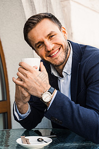 男人喜欢咖啡 英俊的男人在咖啡馆里喝杯咖啡 男性的早晨生活方式 男人坐在咖啡馆的夏日露台上 边喝咖啡边微笑笔记本城市手机屏幕商务图片