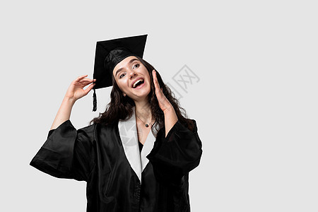 穿着毕业长袍和白底帽的单身女孩大吃一惊 快乐而有趣的年轻女子微笑 学生在单性中获得硕士学位科学家教育成人帽子商业领导者毕业典礼成图片