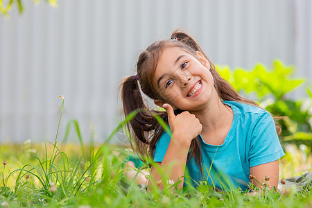 带着两个尾巴的笑着脸红褐发女孩 躺在青草上 在夏花花园图片