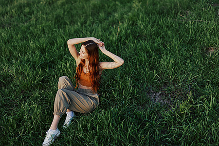 一个美丽的女人 长长的卷卷红色头发 夏天坐在公园里 在日落光下绿草上自由职业者园丁跑步女孩围裙学生微笑衬衫露天女性图片