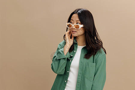 享受着韩国年轻女子穿着卡其绿色衬衫的眼衣时装看得一清二楚 在米色糊面工作室背景上被孤立而无足轻重头发发型女性眼镜广告冲洗黑发护发图片