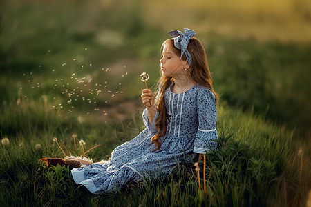 一个穿蓝裙子的女孩坐在草地上 拿着花朵 夏天图片