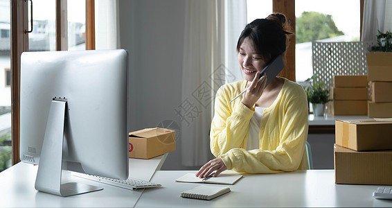 亚洲女性的肖像 电子商务员工坐在办公室里 桌上摆满了包裹 使用笔记本电脑和智能手机 用于中小企业业务 电子商务 技术和交付业务商图片
