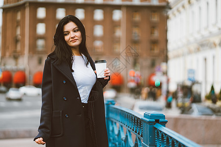 美丽严肃聪明的黑发女孩手里拿着一杯咖啡 走在蓝桥中心的街道上 留着长发的迷人体贴女人独自游荡 沉浸在思绪中图片