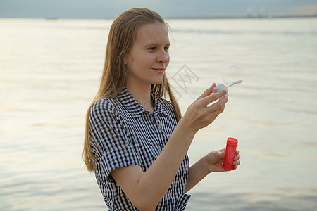 年轻女孩在沙滩上吹起汤泡 欢乐和喜乐的概念背景图片