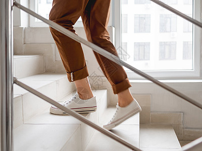 穿着白色运动鞋和卡其裤的女人上楼去她的公寓 在公寓楼的白色楼梯 休闲装 都市时尚 身体锻炼图片