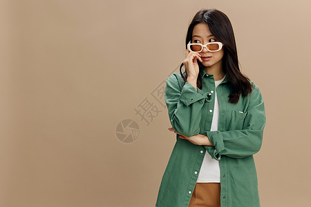 享受着韩国年轻女子穿着卡其绿色衬衫的眼衣时装看得一清二楚 在米色糊面工作室背景上被孤立而无足轻重皮肤美发防晒霜烘干机治疗护发素眼图片