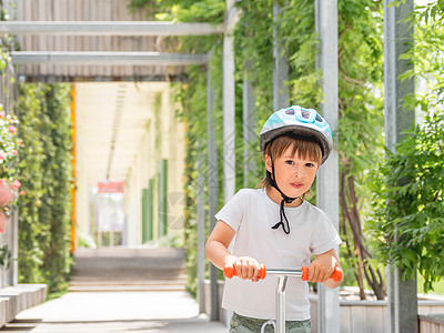 小男孩在滑板公园骑脚踏车 头盔上戴绿叶背景的小孩肖像 夏季训练滑冰操场白色氛围男生树叶学习微笑运动孩子阳光图片