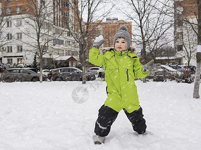 穿着绿色泳衣的笑男孩在树间的雪地院里玩雪球 冬天为孩子们提供休闲活动图片