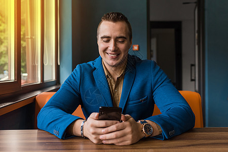 穿着夹克和衬衫的高加索外貌肖像 一个微笑时尚的年轻商务人士坐在手机桌前 望窗外的表情街道短信男人城市经理技术成人电话屏幕细胞图片