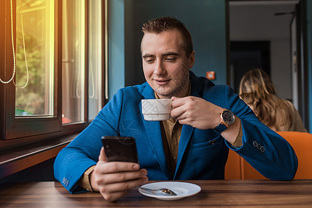 一位心满意足的年轻商务人士 长着可爱的白人肖像 喝着咖啡 午休时用智能手机坐在咖啡馆的桌子旁图片