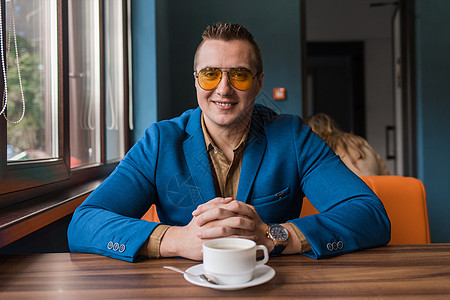 一位面带微笑的商务人士戴着墨镜 在咖啡休息时间闲坐在桌旁 画着一幅时尚的白人肖像 背景是咖啡厅图片