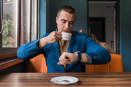 一个忙碌的商务人士 一个穿着西装和衬衫的白人外貌的时尚商务人士 看着时间 谈判迟到了 坐在咖啡馆桌子旁的一杯咖啡旁图片