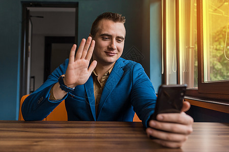 一位年轻时尚的男士 欧洲外貌肖像的商务人士 穿着西装坐在桌子旁 通过智能手机的视频通信交谈 用手势传递问候套装城市商业短信工人技图片