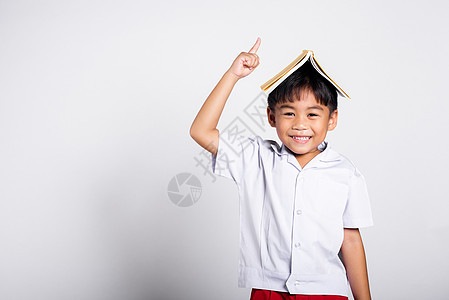 亚洲可爱的蹒跚学步的孩子笑得开心 穿着泰国学生制服的红裤子站着 像屋顶一样把书举过头顶红色童年乐趣学校青春期快乐微笑教育工作服白图片
