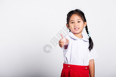 亚洲可爱的小孩 笑着快乐地穿着学生穿泰式校服 红裙子露出拇指举起手指眼镜孩子青少年乐趣学校微笑背包成功教育白色图片
