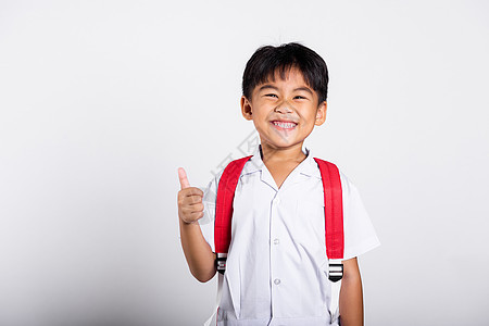 亚洲可爱的小孩 笑着快乐 穿着学生泰文校服 红裤子展示大拇指举起手指冒充幼儿园青少年学校背包乐趣白色男生教育微笑图片