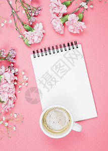 观看咖啡杯上方的咖啡杯空白笔记纸 上面印有康乃馨吉普西雅花花粉红色背景图片