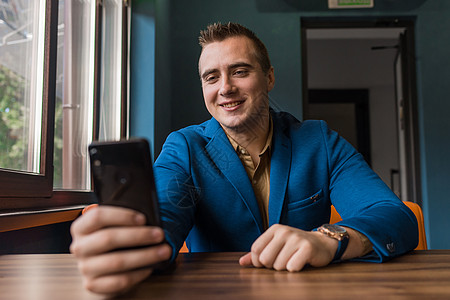一个积极 微笑的欧洲外表的年轻人 一个时尚的商务人士 看着手机或智能手机 自拍或通过视频链接交谈图片