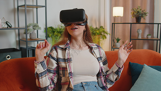 年轻女孩在家里使用虚拟现实耳机眼镜玩3D视频游戏 手举手做手势虚拟现实闲暇互联网技术女性风镜娱乐创新休息房子图片